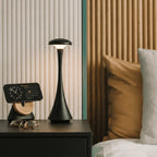 Luminária de mesa Elysium Touch Larvivaz acesa sobre um móvel de cabeceira, decorando um quarto moderno.