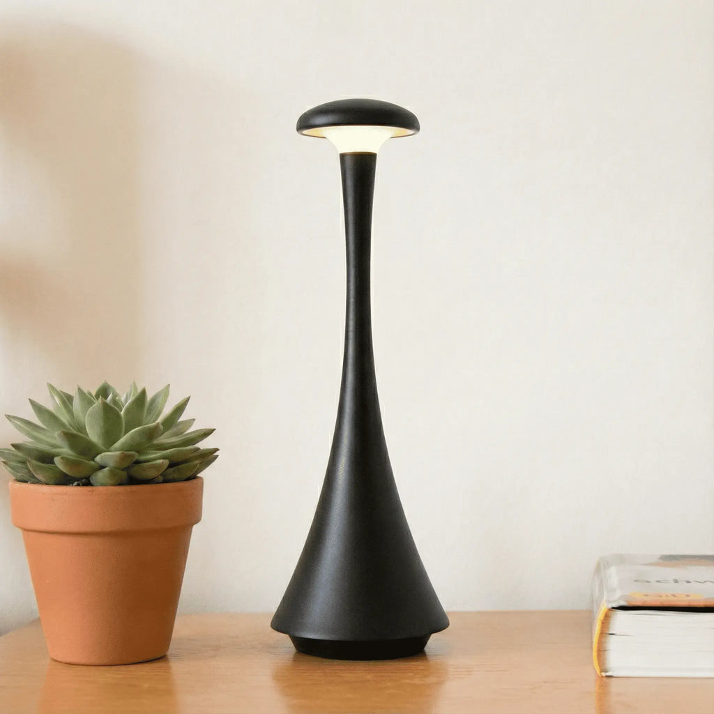 Luminária de mesa Elysium Touch preta sobre uma mesa de madeira, com uma planta ao lado, em um ambiente de sala de estar.