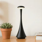 Luminária de mesa Elysium Touch preta sobre uma mesa de madeira, com uma planta ao lado, em um ambiente de sala de estar.